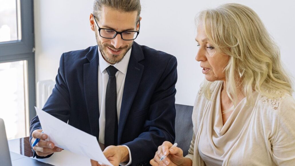 A man in a suit and a woman with blonde hair going through printed documents together at a desk