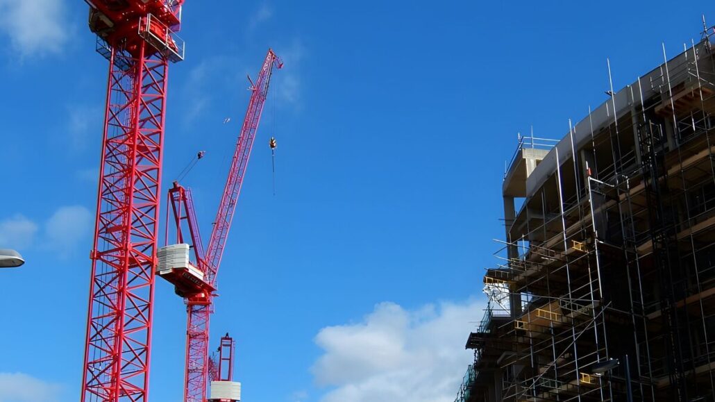 Red tower cranes beside a scaffolded building under construction in Islington, London